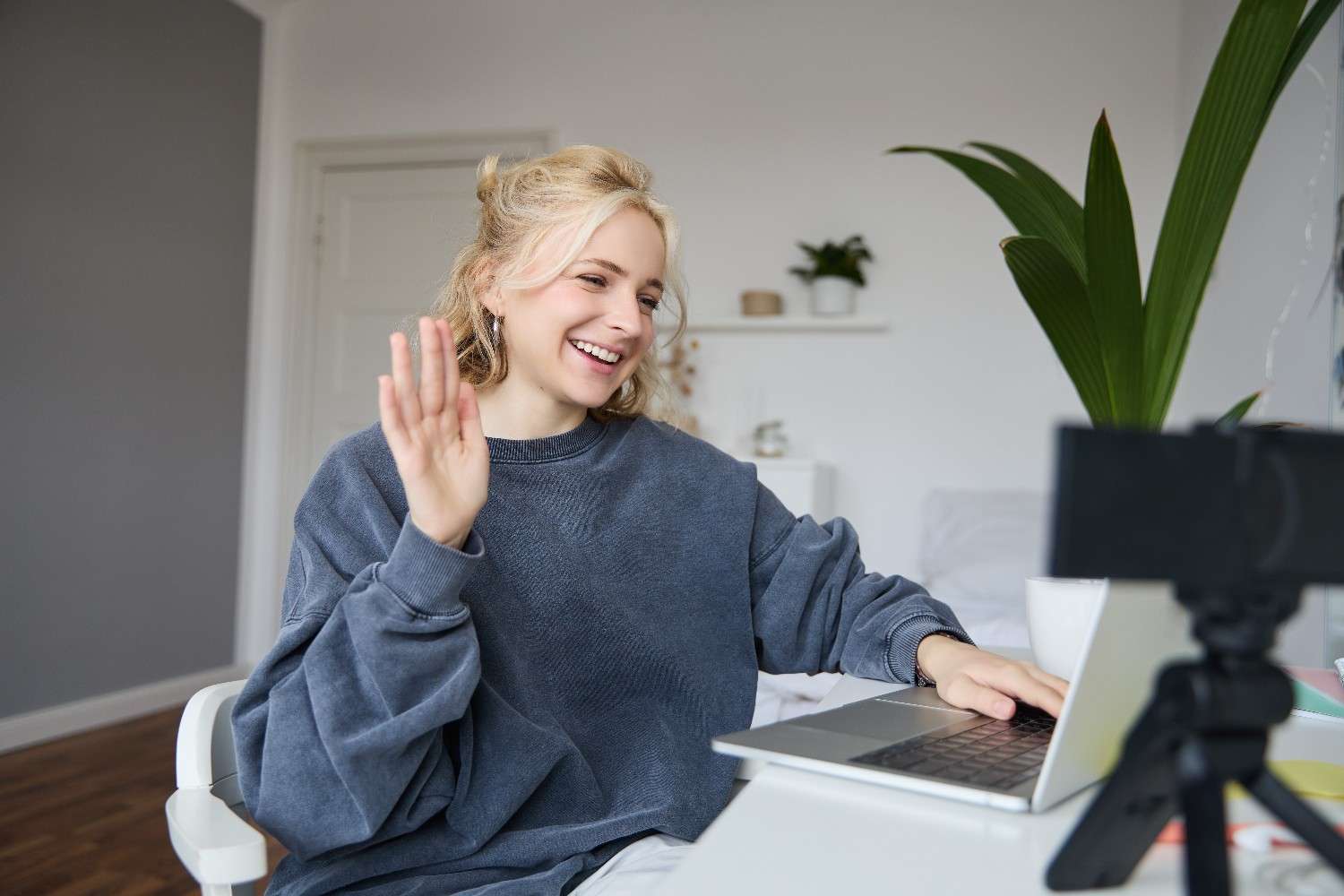 Person smiling and waving at a laptop during a video call